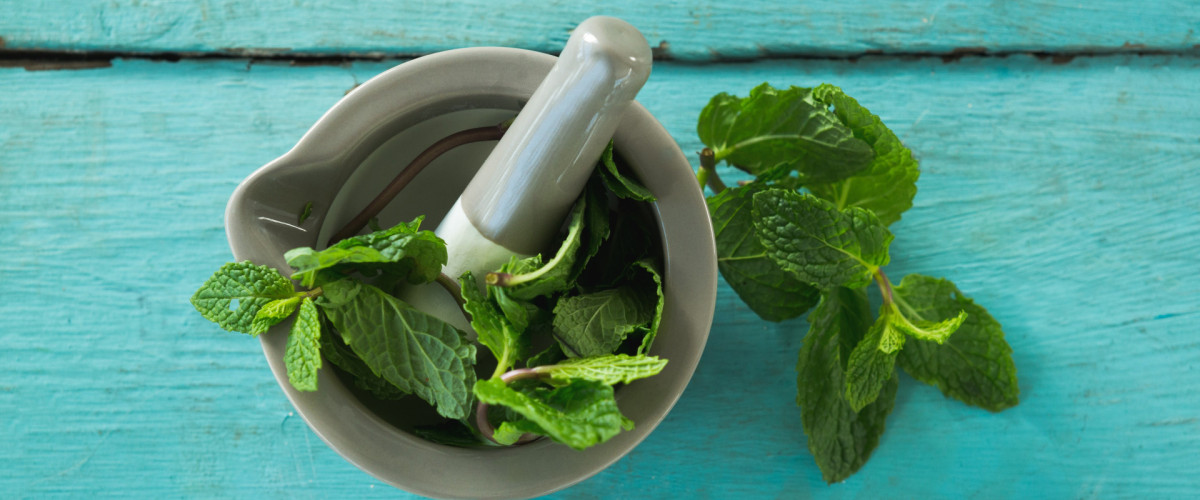 Minzblätter mit Mörser und Stößel auf einem Holztisch